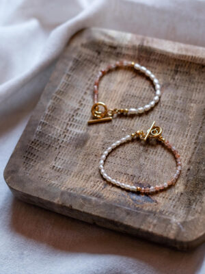 Dwie bransoletki z pereł naturalnych i kamieni słonecznych ze złotym zapięciem ułożone na drewnianej podstawce