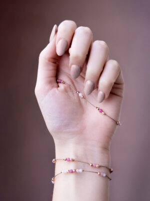 Kobieca dłoń ubrana w trzy bransoletki z opali oraz różowych turmalinów