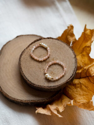 Dwa pierścionki na gumce z perłami naturalnymi i kamieniami słonecznymi ułożone na drewnianych podstawkach