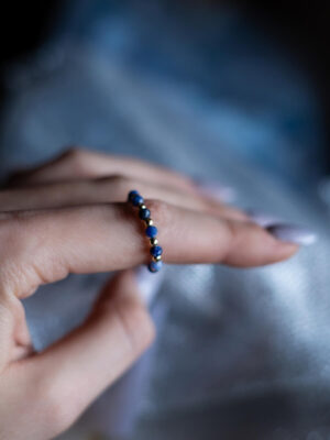 Niebieski pierścionek z sodalitów i złotych hematytów zaprezentowany na palcu