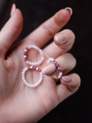 Trzy pierścionki z opali i różowych turmalinów ułożone na kobiecej dłoni